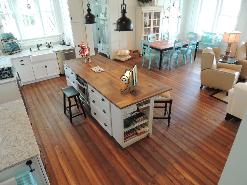 Maritim inredning av ett stort kök, med mellanmörkt trägolv, en rustik diskho, släta luckor, vita skåp, granitbänkskiva, vitt stänkskydd, rostfria vitvaror, en köksö och brunt golv