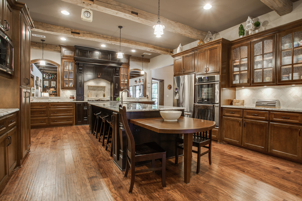 Large mountain style u-shaped medium tone wood floor and brown floor eat-in kitchen photo in Dallas with stone tile backsplash, stainless steel appliances, glass-front cabinets, medium tone wood cabinets, granite countertops and an island