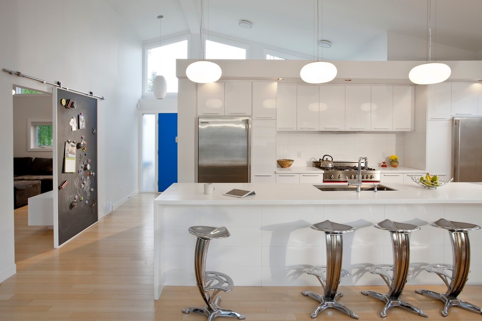 Photo of a modern galley kitchen in Calgary with stainless steel appliances, a single-bowl sink, flat-panel cabinets, white cabinets and white splashback.