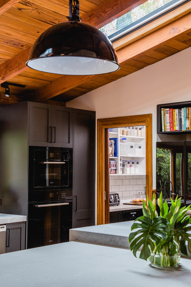 Rustik inredning av ett stort grå grått kök, med en undermonterad diskho, skåp i shakerstil, svarta skåp, bänkskiva i kvarts, vitt stänkskydd, stänkskydd i terrakottakakel, svarta vitvaror, mellanmörkt trägolv, en köksö och brunt golv