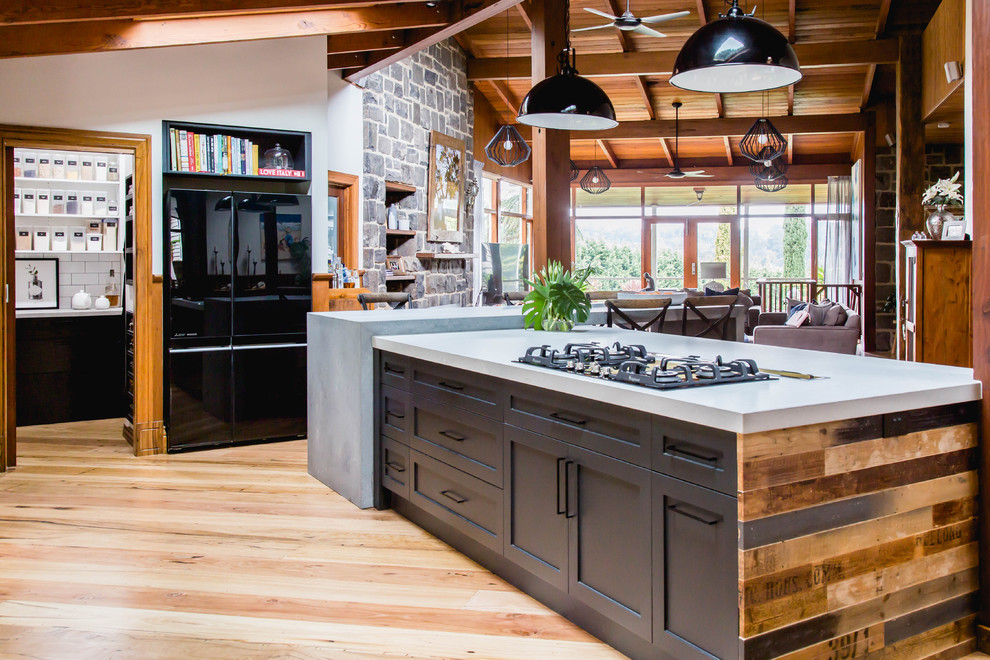 Idéer för ett stort rustikt grå kök, med en undermonterad diskho, skåp i shakerstil, svarta skåp, bänkskiva i kvarts, vitt stänkskydd, stänkskydd i terrakottakakel, svarta vitvaror, mellanmörkt trägolv, en köksö och brunt golv