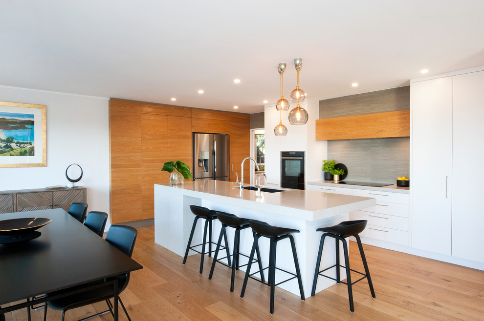 Photo of a contemporary l-shaped kitchen in Auckland with a double-bowl sink, engineered stone countertops, grey splashback, ceramic splashback, stainless steel appliances, light hardwood flooring and an island.