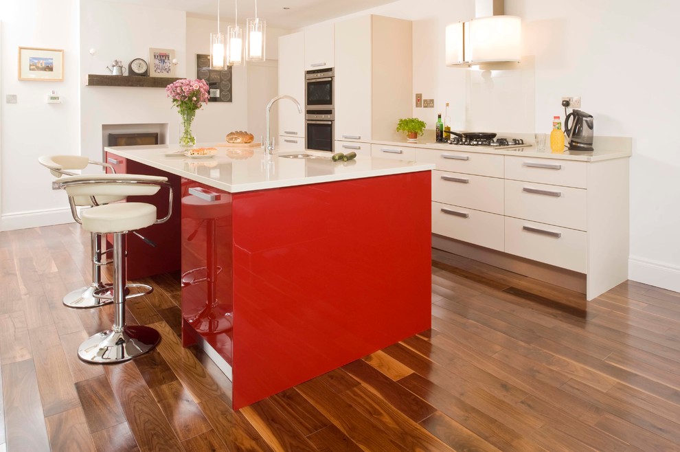 Immagine di una grande cucina minimal con lavello sottopiano, ante lisce, ante rosse, top in quarzo composito, paraspruzzi bianco, paraspruzzi con lastra di vetro e parquet scuro