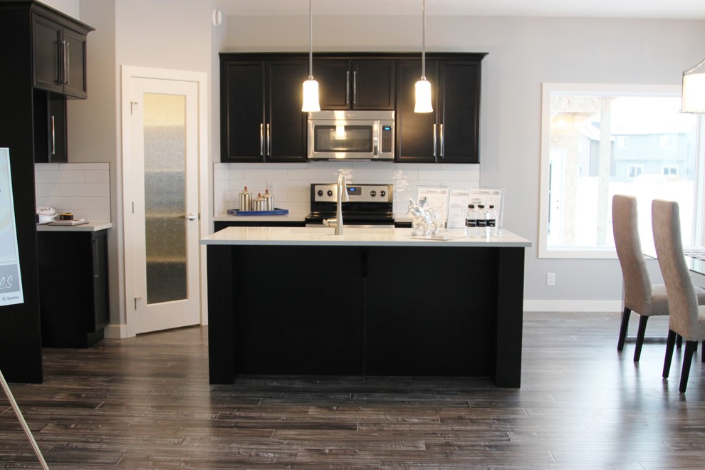 Large minimalist l-shaped dark wood floor eat-in kitchen photo in Calgary with an undermount sink, recessed-panel cabinets, black cabinets, granite countertops, white backsplash, subway tile backsplash, stainless steel appliances and an island