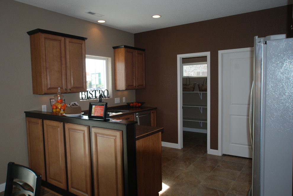 Klassisk inredning av ett kök och matrum, med en dubbel diskho, luckor med infälld panel, skåp i mellenmörkt trä, laminatbänkskiva, rostfria vitvaror, laminatgolv och en halv köksö