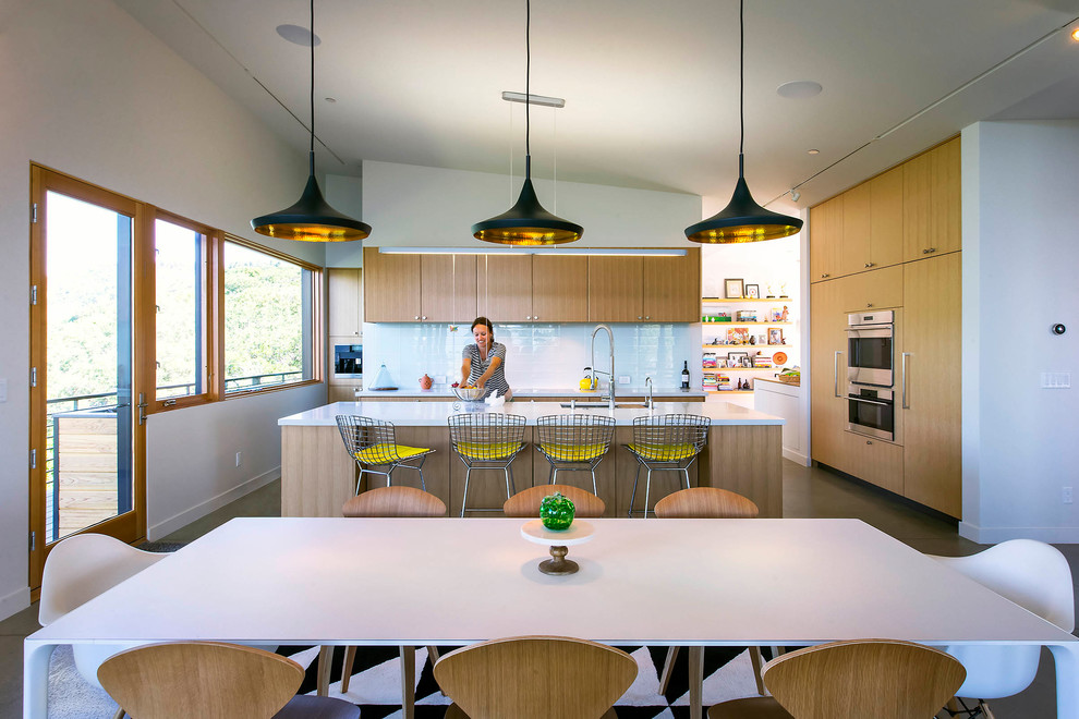 Bild på ett mellanstort funkis kök med öppen planlösning, med en undermonterad diskho, släta luckor, skåp i ljust trä, bänkskiva i kvarts, blått stänkskydd, stänkskydd i glaskakel, rostfria vitvaror, betonggolv, en köksö och grått golv