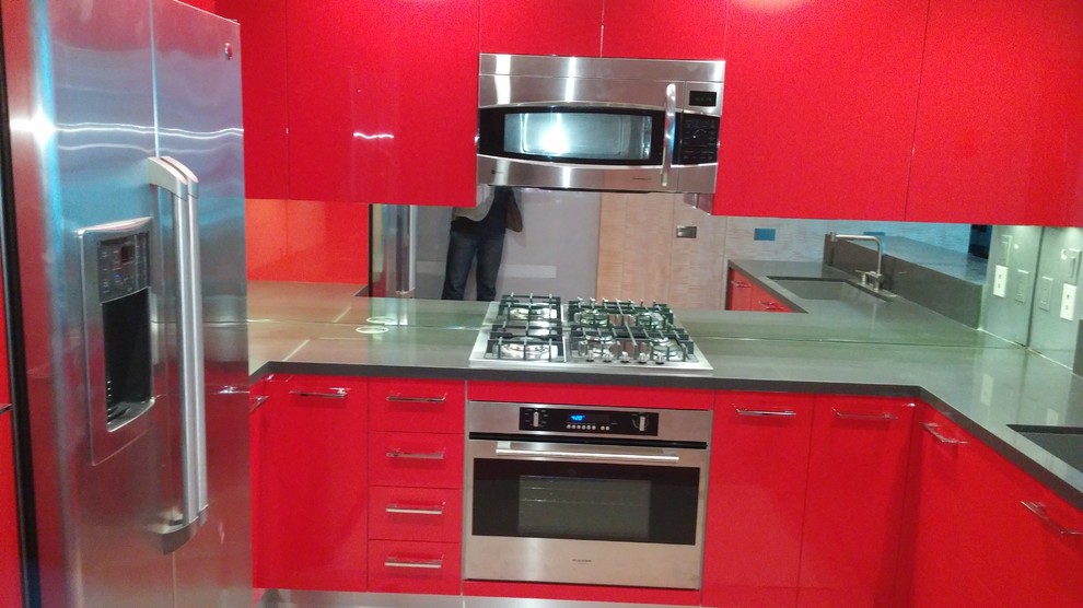 Bild på ett litet funkis kök, med släta luckor, röda skåp, bänkskiva i kvarts, stänkskydd med metallisk yta, glaspanel som stänkskydd, rostfria vitvaror, målat trägolv, en halv köksö och en undermonterad diskho