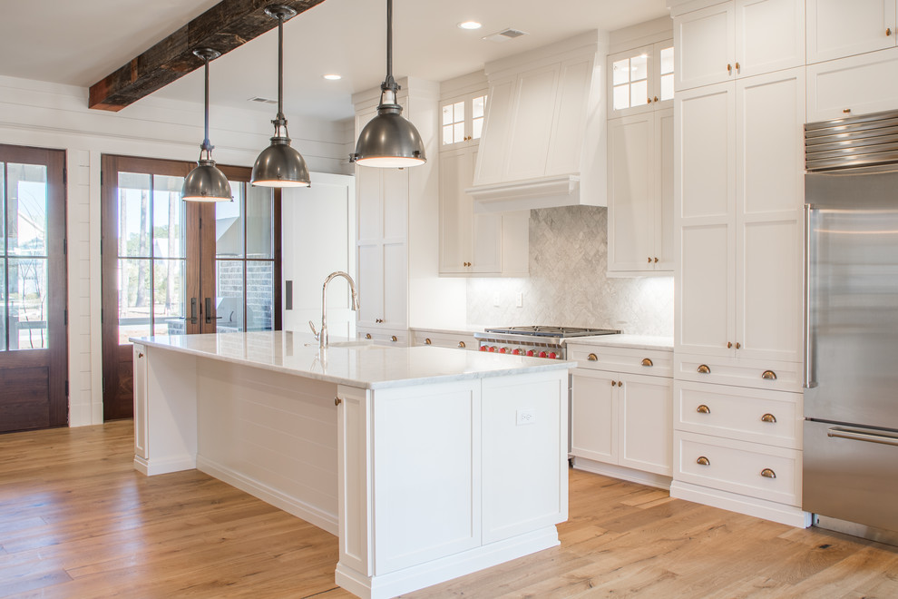 Medium sized country single-wall kitchen/diner in Atlanta with a belfast sink, shaker cabinets, white cabinets, marble worktops, white splashback, marble splashback, stainless steel appliances, medium hardwood flooring, an island and brown floors.