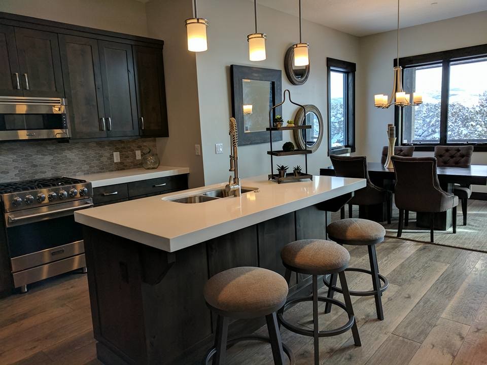 Design ideas for a large contemporary single-wall kitchen/diner in Salt Lake City with a double-bowl sink, shaker cabinets, dark wood cabinets, composite countertops, grey splashback, porcelain splashback, stainless steel appliances, light hardwood flooring, an island and brown floors.