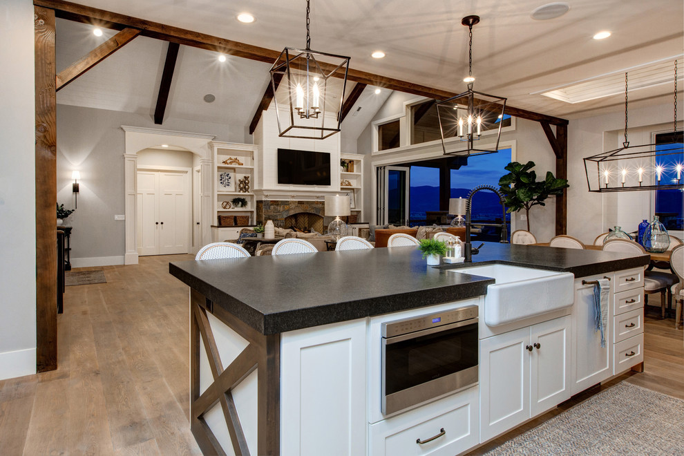 Photo of a large farmhouse single-wall open plan kitchen in Salt Lake City with a belfast sink, shaker cabinets, white cabinets, soapstone worktops, white splashback, metro tiled splashback, stainless steel appliances, medium hardwood flooring and an island.