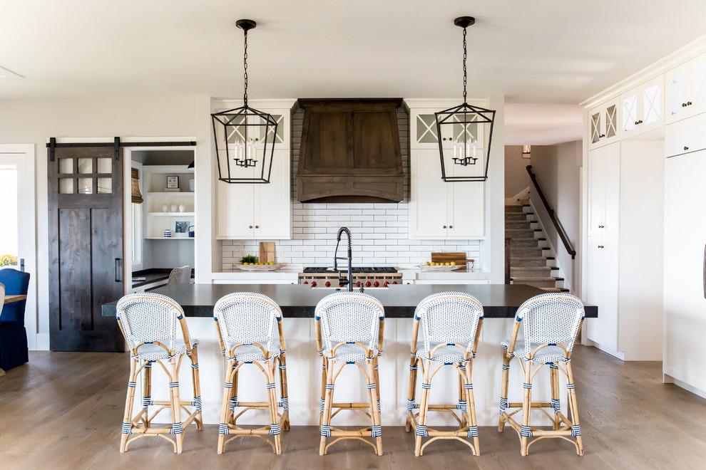 Inspiration for a large farmhouse single-wall medium tone wood floor open concept kitchen remodel in Salt Lake City with a farmhouse sink, white cabinets, white backsplash, subway tile backsplash, an island, shaker cabinets, soapstone countertops, stainless steel appliances and black countertops