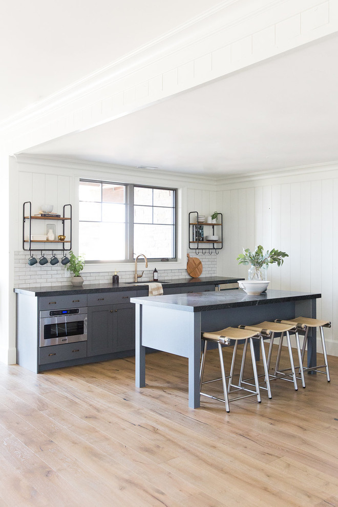 Immagine di una piccola cucina country con ante blu, paraspruzzi bianco, elettrodomestici in acciaio inossidabile, parquet scuro e top grigio