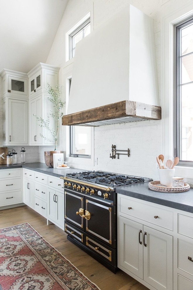 Große Landhausstil Küche in L-Form mit weißen Schränken, Küchenrückwand in Weiß, schwarzen Elektrogeräten, dunklem Holzboden, Kücheninsel und grauer Arbeitsplatte in Salt Lake City