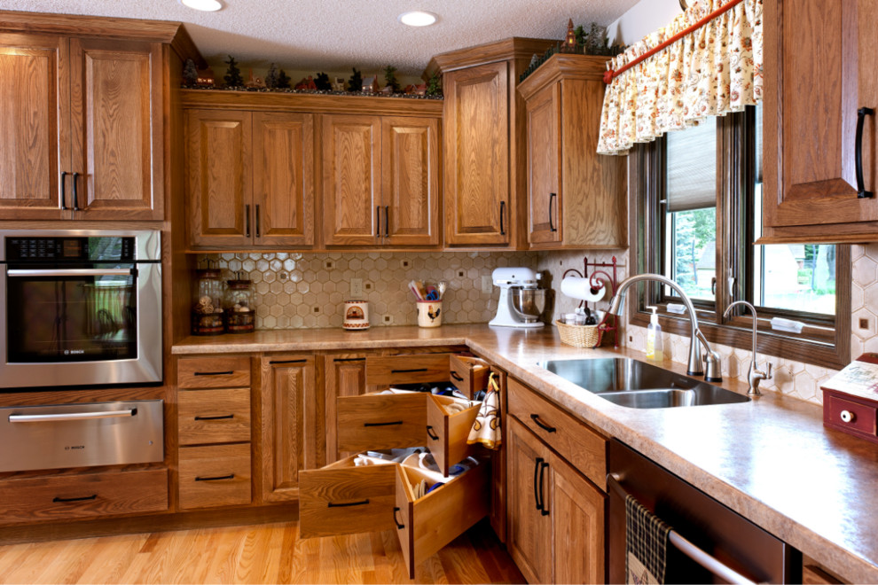 Bild på ett stort amerikanskt kök, med en dubbel diskho, luckor med upphöjd panel, skåp i mörkt trä, beige stänkskydd, stänkskydd i keramik, rostfria vitvaror, ljust trägolv, en köksö och beiget golv