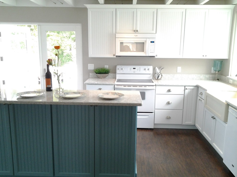 Example of a mid-sized beach style dark wood floor and brown floor kitchen design in Tampa with a farmhouse sink, louvered cabinets, white cabinets, granite countertops, white appliances and an island