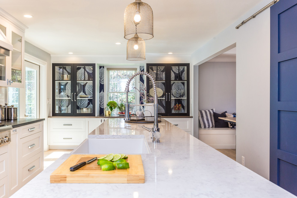 Example of a transitional galley light wood floor and brown floor eat-in kitchen design in Manchester with a farmhouse sink, shaker cabinets, white cabinets, soapstone countertops, white backsplash, ceramic backsplash, stainless steel appliances and an island
