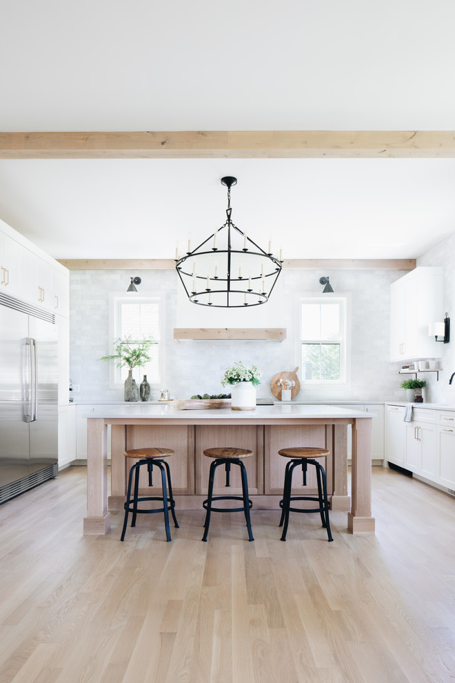 Farmhouse u-shaped light wood floor and beige floor eat-in kitchen photo in Chicago with an undermount sink, shaker cabinets, white cabinets, gray backsplash, stainless steel appliances, an island and white countertops