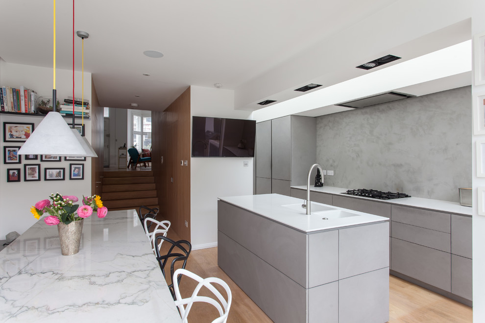Inspiration for a mid-sized contemporary single-wall light wood floor and beige floor kitchen remodel in London with a double-bowl sink, flat-panel cabinets, gray cabinets, gray backsplash, an island and white countertops