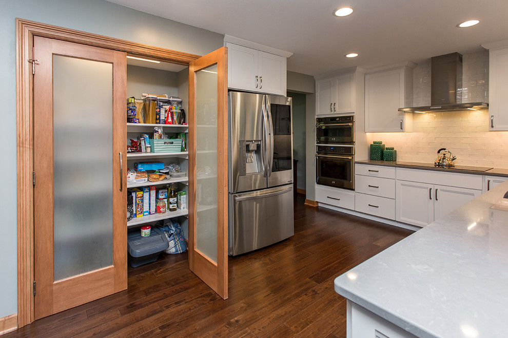 Large transitional u-shaped medium tone wood floor and brown floor eat-in kitchen photo in Other with an undermount sink, recessed-panel cabinets, white cabinets, quartz countertops, white backsplash, ceramic backsplash, stainless steel appliances and an island