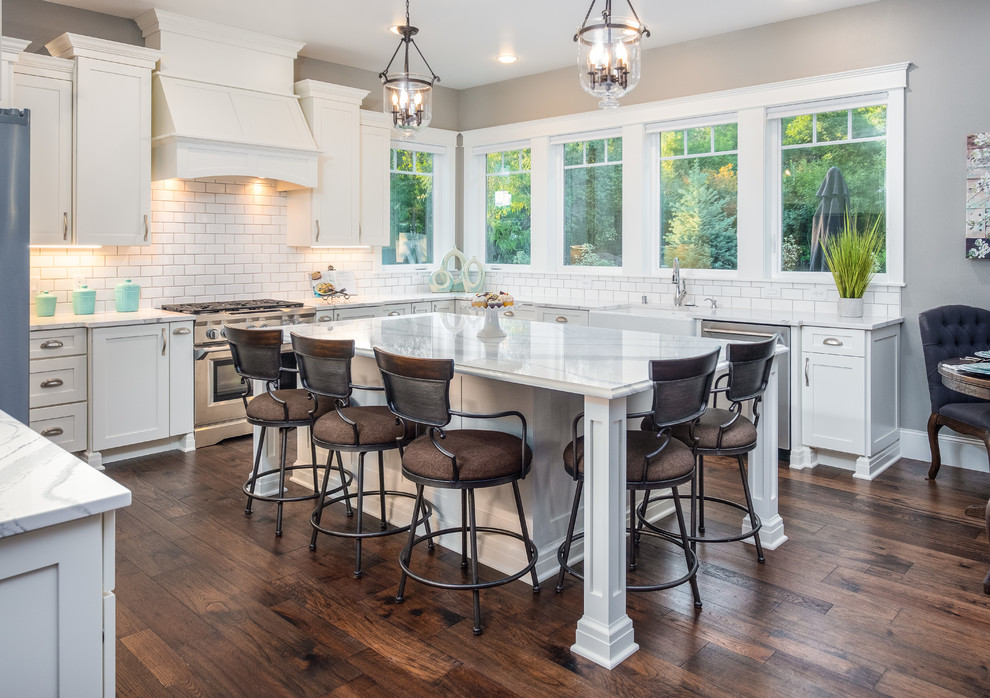 Large elegant dark wood floor kitchen photo in Other with a farmhouse sink, shaker cabinets, white cabinets, quartzite countertops, white backsplash, subway tile backsplash, stainless steel appliances, an island and white countertops