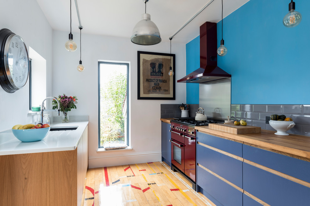 Cette image montre une petite cuisine parallèle design avec un évier encastré, un placard à porte plane, des portes de placard bleues, une crédence grise, une crédence en carrelage métro, parquet clair et un sol beige.