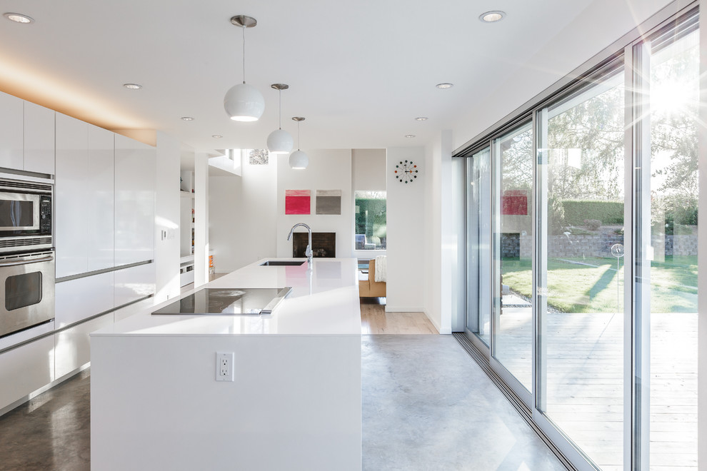Photo of a medium sized contemporary galley open plan kitchen in Seattle with flat-panel cabinets, white cabinets, stainless steel appliances, concrete flooring and an island.