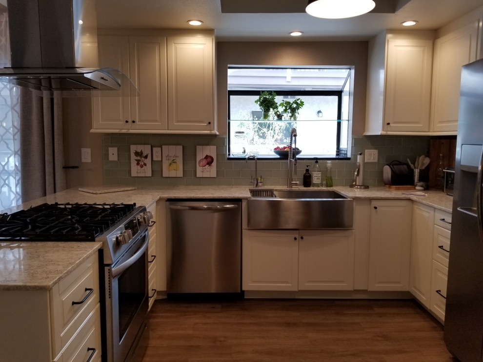 Inspiration for a small coastal u-shaped vinyl floor and brown floor enclosed kitchen remodel in Los Angeles with a farmhouse sink, raised-panel cabinets, yellow cabinets, solid surface countertops, green backsplash, glass tile backsplash, stainless steel appliances, a peninsula and multicolored countertops