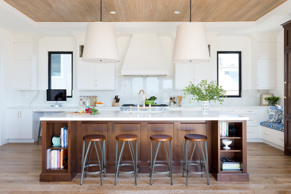 This is an example of a nautical kitchen in Los Angeles with shaker cabinets, white cabinets, white splashback, medium hardwood flooring and an island.