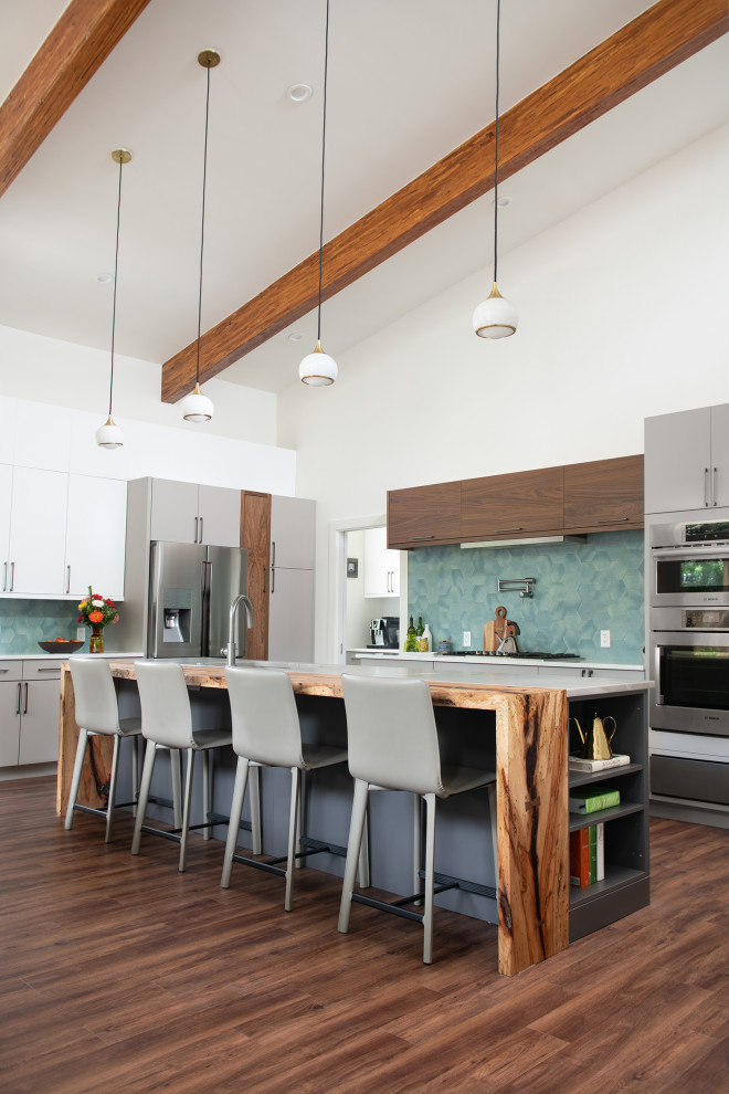 Mid-Century Küche in L-Form mit flächenbündigen Schrankfronten, grauen Schränken, Küchenrückwand in Blau, Küchengeräten aus Edelstahl, dunklem Holzboden, Kücheninsel, braunem Boden, grauer Arbeitsplatte, freigelegten Dachbalken und gewölbter Decke in Houston