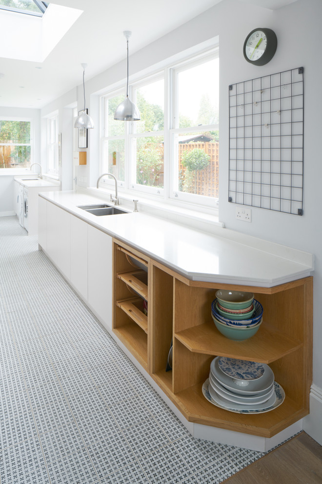 Design ideas for a large contemporary galley enclosed kitchen in London with an integrated sink, white cabinets, white splashback, stainless steel appliances, porcelain flooring and no island.