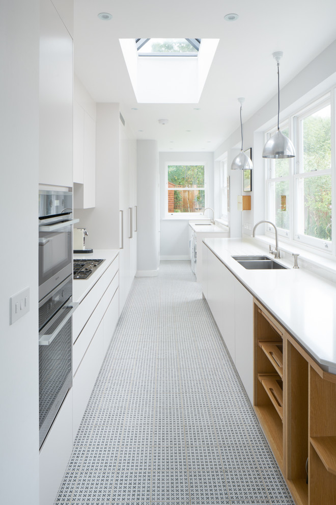Inspiration for a large contemporary galley enclosed kitchen in London with an integrated sink, white cabinets, white splashback, stainless steel appliances, porcelain flooring and no island.