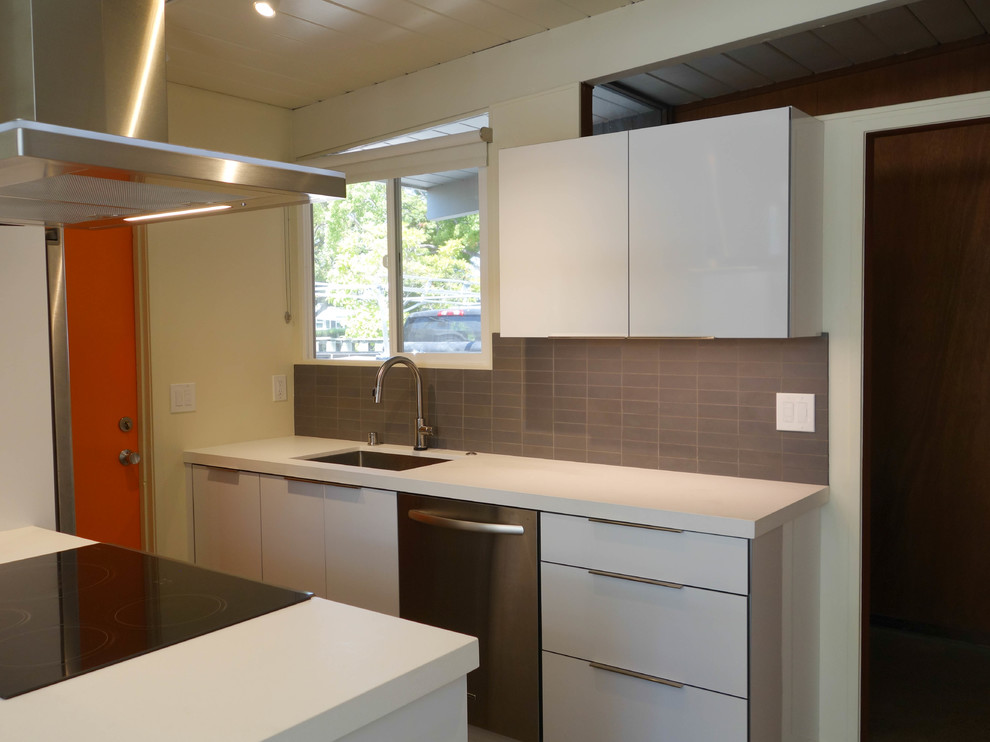 This is an example of a medium sized retro galley kitchen/diner in San Francisco with a submerged sink, flat-panel cabinets, white cabinets, engineered stone countertops, grey splashback, ceramic splashback, stainless steel appliances, concrete flooring, an island, grey floors and white worktops.