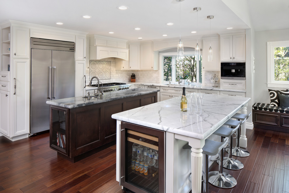 Large classic l-shaped kitchen in San Francisco with recessed-panel cabinets, white cabinets, marble worktops, white splashback, multiple islands, a submerged sink, metro tiled splashback, stainless steel appliances and dark hardwood flooring.