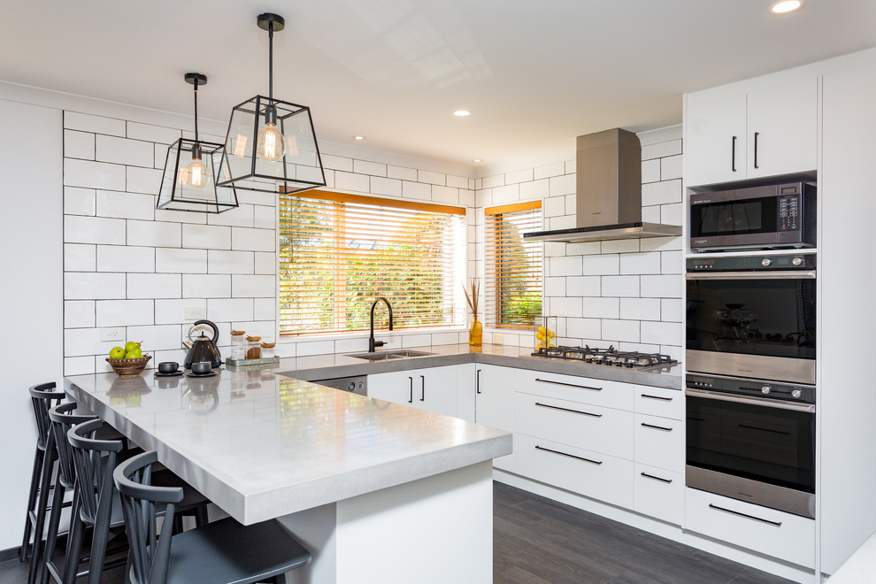 Mid-sized minimalist u-shaped dark wood floor and brown floor enclosed kitchen photo in Christchurch with an undermount sink, flat-panel cabinets, white cabinets, concrete countertops, white backsplash, subway tile backsplash, stainless steel appliances, a peninsula and gray countertops
