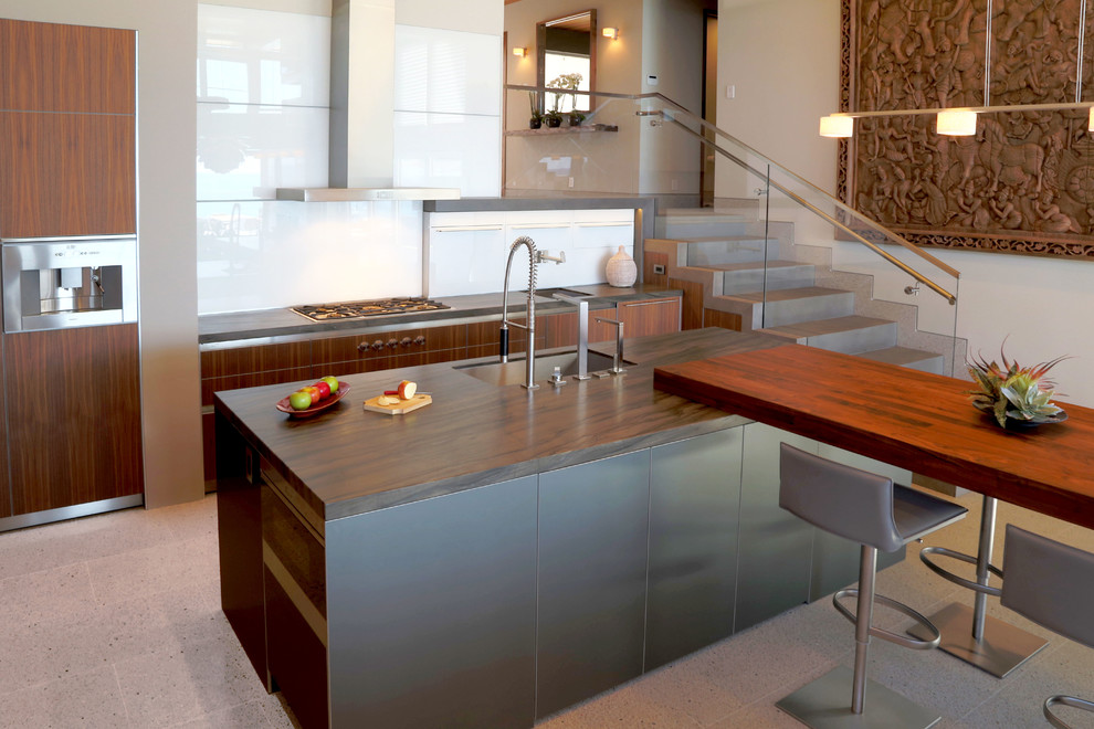 Photo of a contemporary galley kitchen in Orange County with a submerged sink, flat-panel cabinets, dark wood cabinets, white splashback, stainless steel appliances and an island.