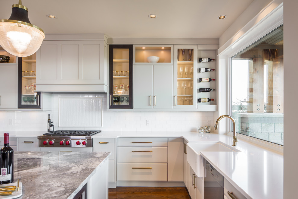 Mid-sized transitional u-shaped brown floor and medium tone wood floor eat-in kitchen photo in Vancouver with a farmhouse sink, flat-panel cabinets, gray cabinets, quartz countertops, white backsplash, ceramic backsplash, stainless steel appliances, an island and gray countertops