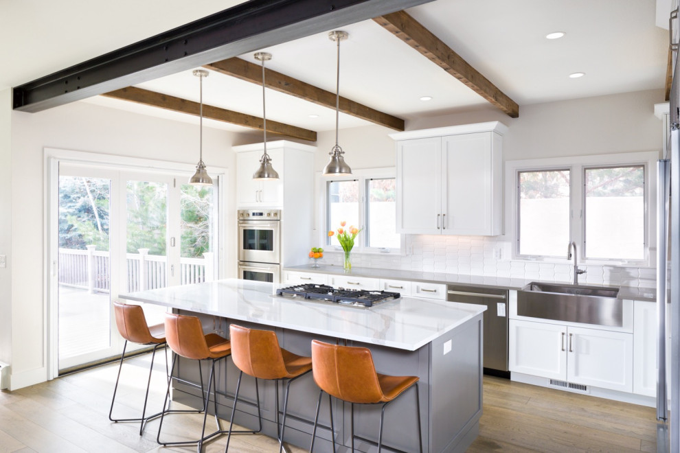 Example of a large urban l-shaped medium tone wood floor and beige floor eat-in kitchen design in Denver with a drop-in sink, recessed-panel cabinets, white cabinets, quartz countertops, white backsplash, ceramic backsplash, stainless steel appliances, an island and gray countertops