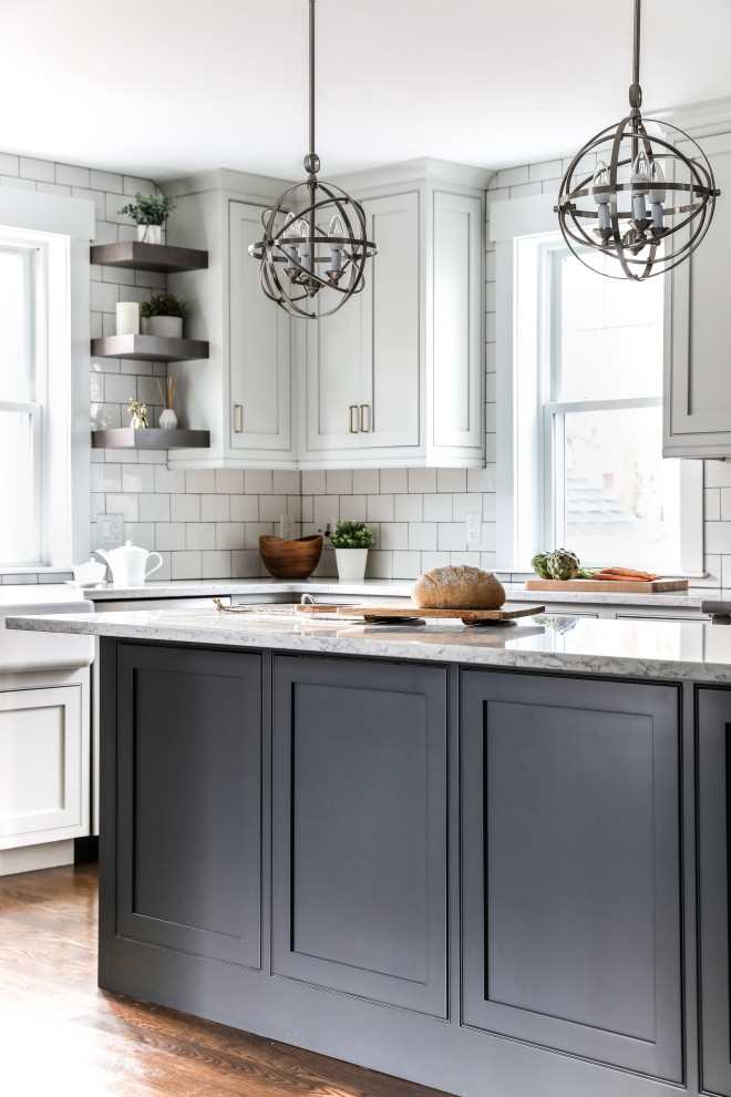 Klassisk inredning av ett grå grått kök, med en rustik diskho, luckor med profilerade fronter, vita skåp, bänkskiva i kvarts, vitt stänkskydd, stänkskydd i tunnelbanekakel, rostfria vitvaror, mellanmörkt trägolv, en köksö och brunt golv