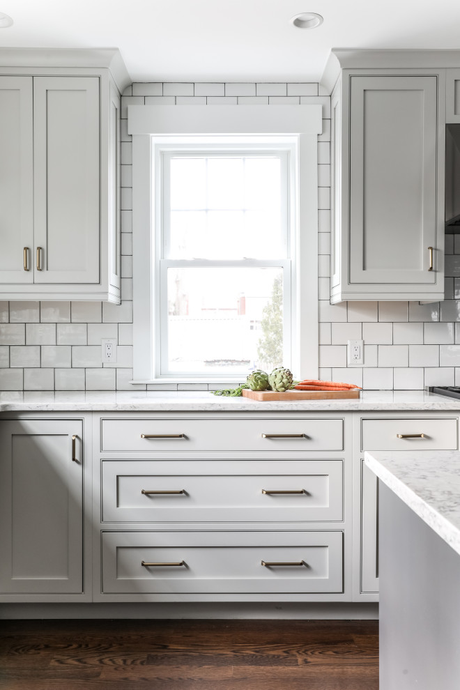 This is an example of a traditional l-shaped kitchen/diner in Boston with a belfast sink, beaded cabinets, white cabinets, engineered stone countertops, white splashback, metro tiled splashback, stainless steel appliances, medium hardwood flooring, an island, brown floors and grey worktops.