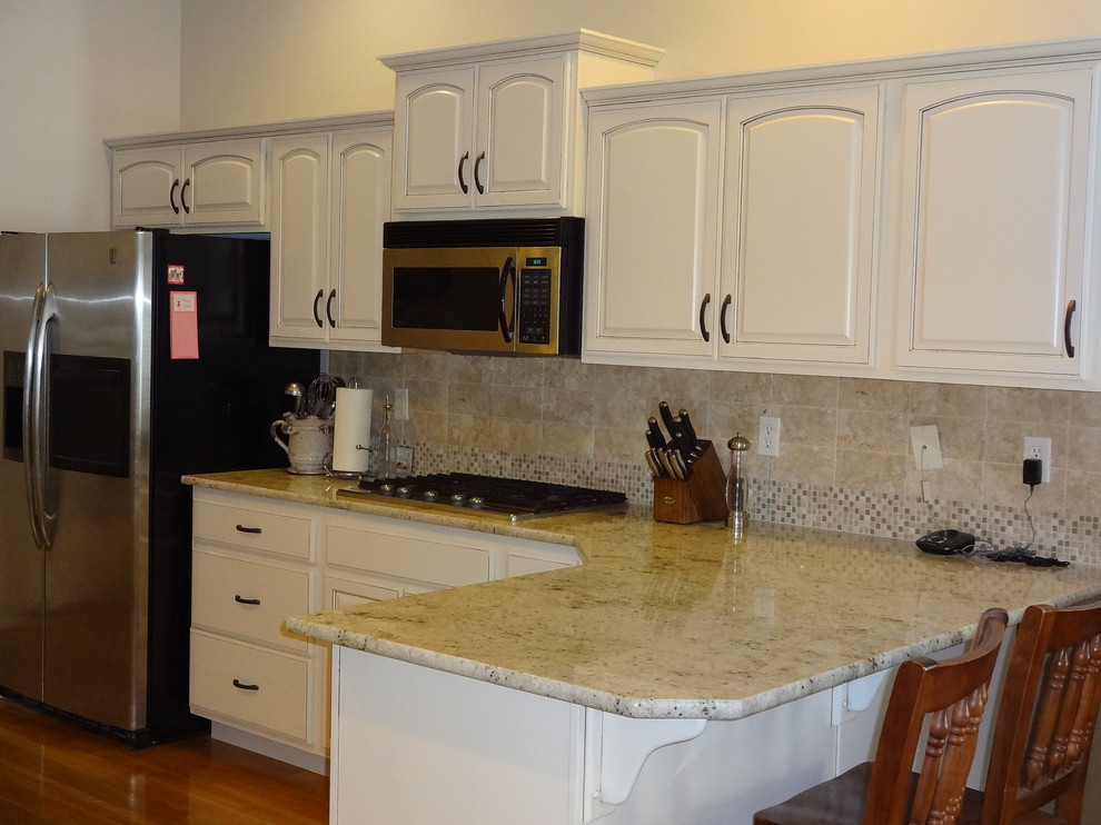 Exemple d'une grande cuisine chic avec un placard avec porte à panneau surélevé, des portes de placard blanches, un plan de travail en granite, une crédence marron, un électroménager en acier inoxydable et un sol en bois brun.
