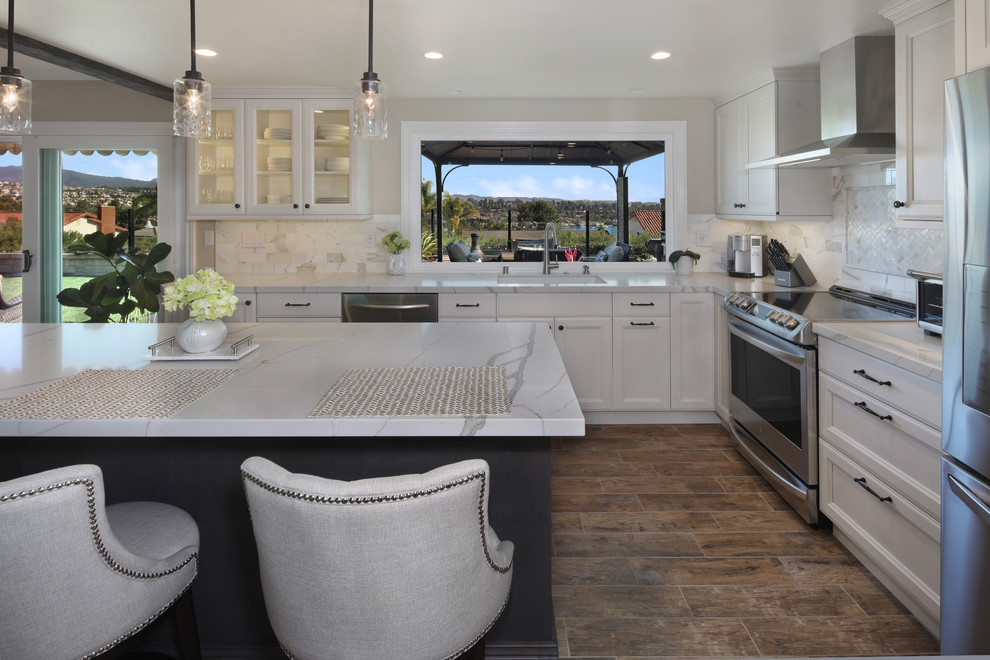 Inspiration for a mid-sized eclectic l-shaped porcelain tile and brown floor open concept kitchen remodel in Orange County with an undermount sink, recessed-panel cabinets, white cabinets, quartz countertops, gray backsplash, marble backsplash, stainless steel appliances, an island and white countertops