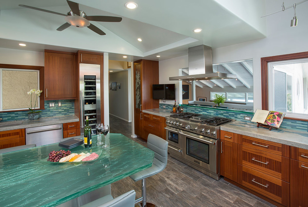 Eat-in kitchen - large tropical porcelain tile eat-in kitchen idea in Hawaii with an undermount sink, shaker cabinets, medium tone wood cabinets, concrete countertops, blue backsplash, glass tile backsplash, stainless steel appliances and no island