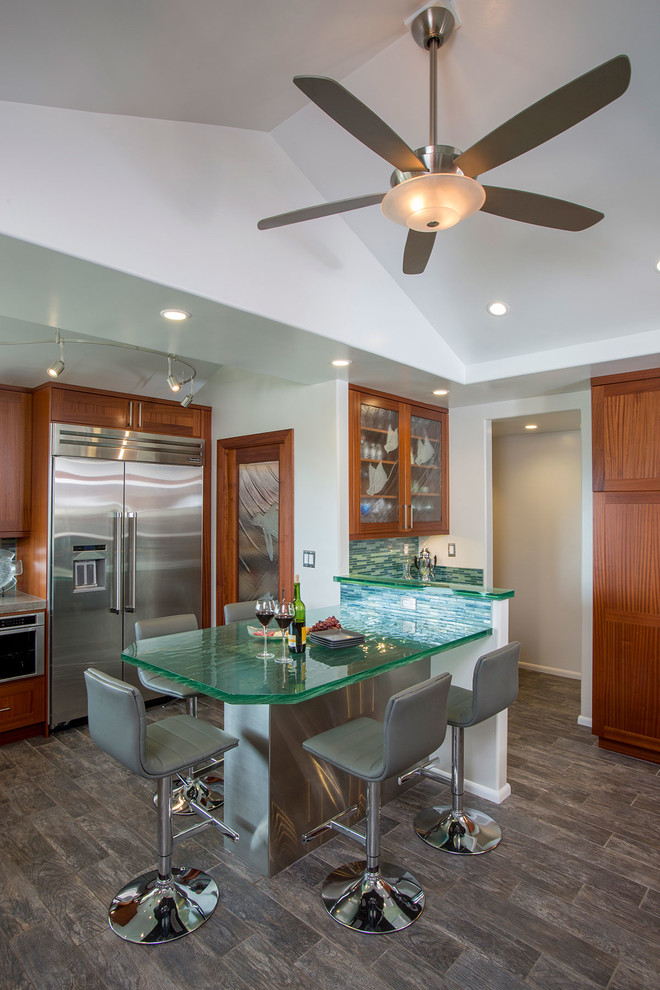 Eat-in kitchen - large tropical porcelain tile eat-in kitchen idea in Hawaii with an undermount sink, shaker cabinets, medium tone wood cabinets, glass countertops, green backsplash, glass tile backsplash, stainless steel appliances and no island