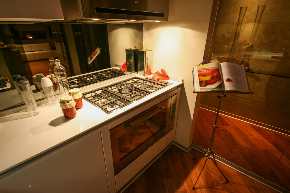 Foto di una cucina a L contemporanea chiusa con ante lisce, ante bianche, top in superficie solida, paraspruzzi a specchio e pavimento in legno massello medio
