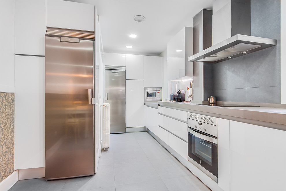Enclosed kitchen - mid-sized contemporary galley ceramic tile enclosed kitchen idea in Madrid with flat-panel cabinets, white cabinets, solid surface countertops, gray backsplash, ceramic backsplash, stainless steel appliances and no island