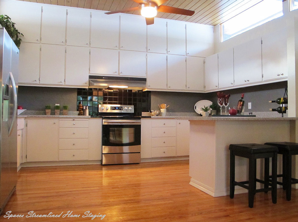 Bild på ett mellanstort retro kök, med en dubbel diskho, släta luckor, vita skåp, laminatbänkskiva, grått stänkskydd, stänkskydd i keramik, rostfria vitvaror, ljust trägolv och en halv köksö