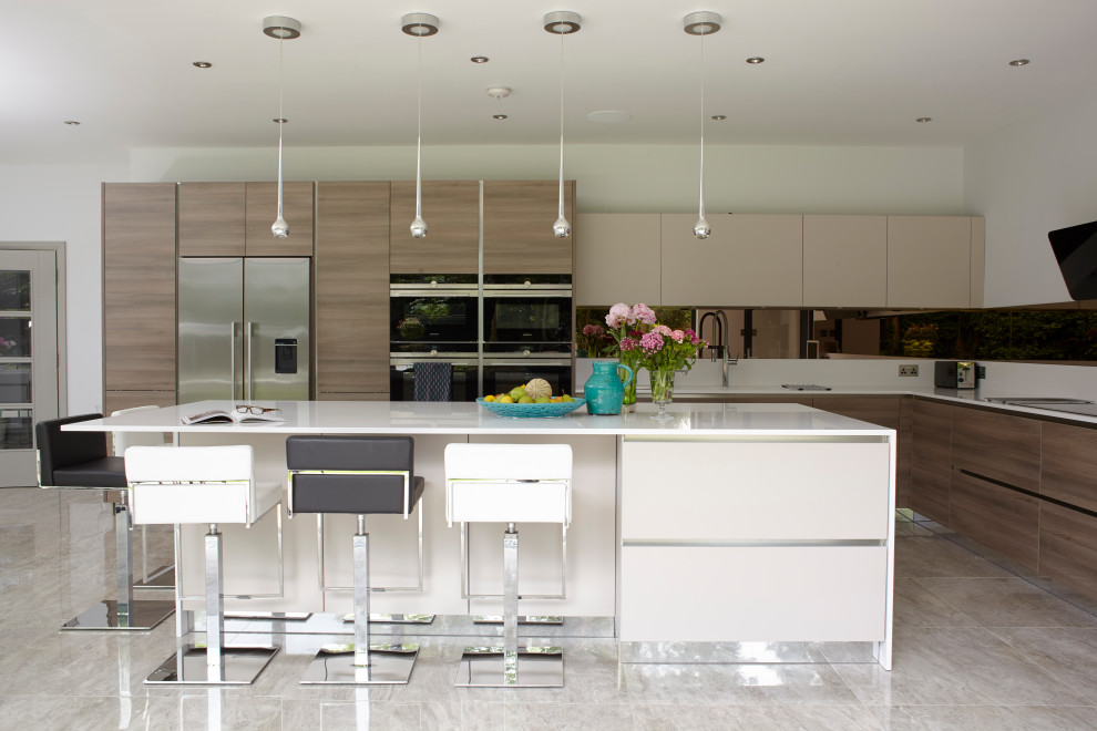 Moderne Küche in L-Form mit flächenbündigen Schrankfronten, beigen Schränken, Rückwand aus Spiegelfliesen, Küchengeräten aus Edelstahl, Kücheninsel, beigem Boden und weißer Arbeitsplatte in Buckinghamshire