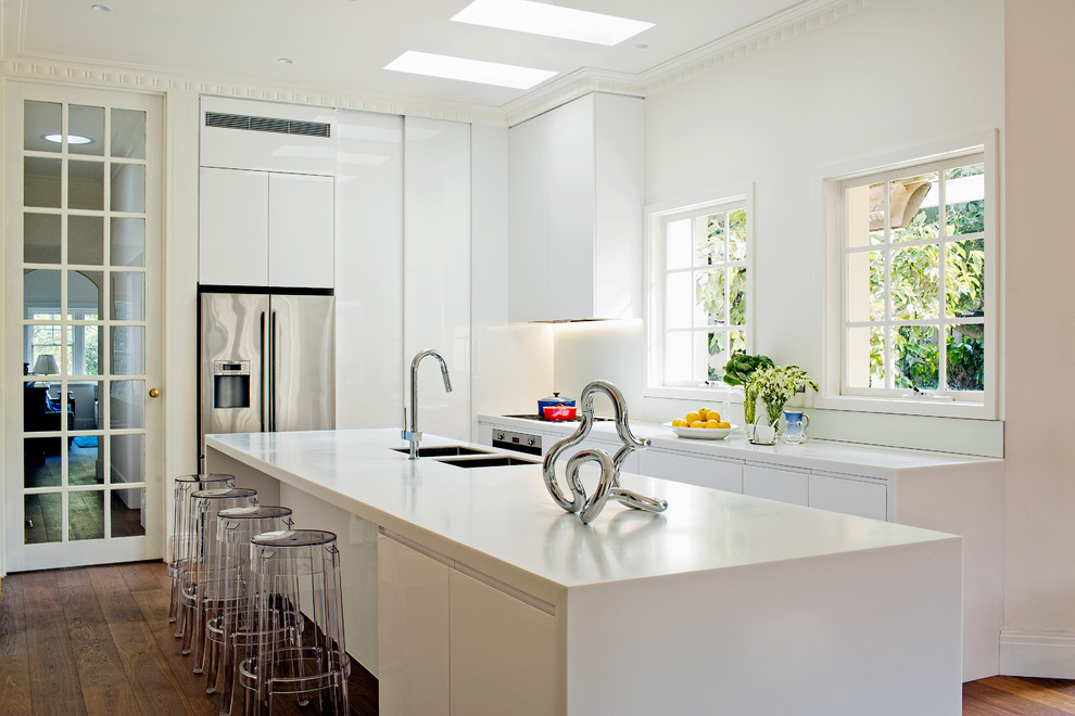 Immagine di una grande cucina design con lavello a doppia vasca, ante lisce, ante bianche, elettrodomestici in acciaio inossidabile, top in superficie solida, paraspruzzi bianco e paraspruzzi con lastra di vetro