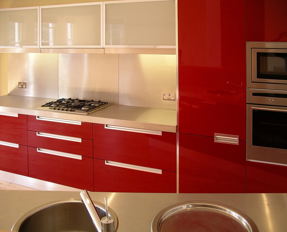 Inredning av ett modernt litet kök, med röda skåp, bänkskiva i rostfritt stål, stänkskydd med metallisk yta, stänkskydd i metallkakel, rostfria vitvaror och ljust trägolv