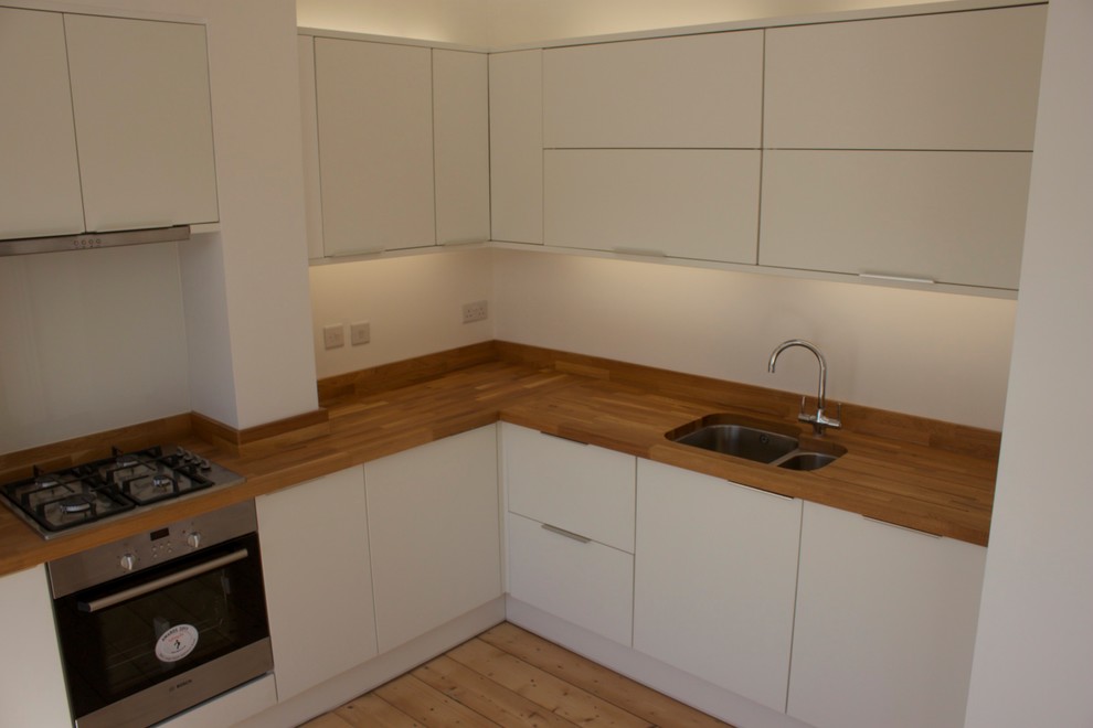 Photo of a medium sized modern l-shaped kitchen/diner in Other with a submerged sink, flat-panel cabinets, white cabinets, wood worktops, stainless steel appliances, light hardwood flooring and no island.
